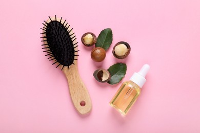 Photo of Delicious organic Macadamia nuts, natural oil, brush and green leaves on pink background, flat lay