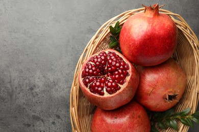 Fresh pomegranates and green leaves in wicker basket on grey table, top view. Space for text