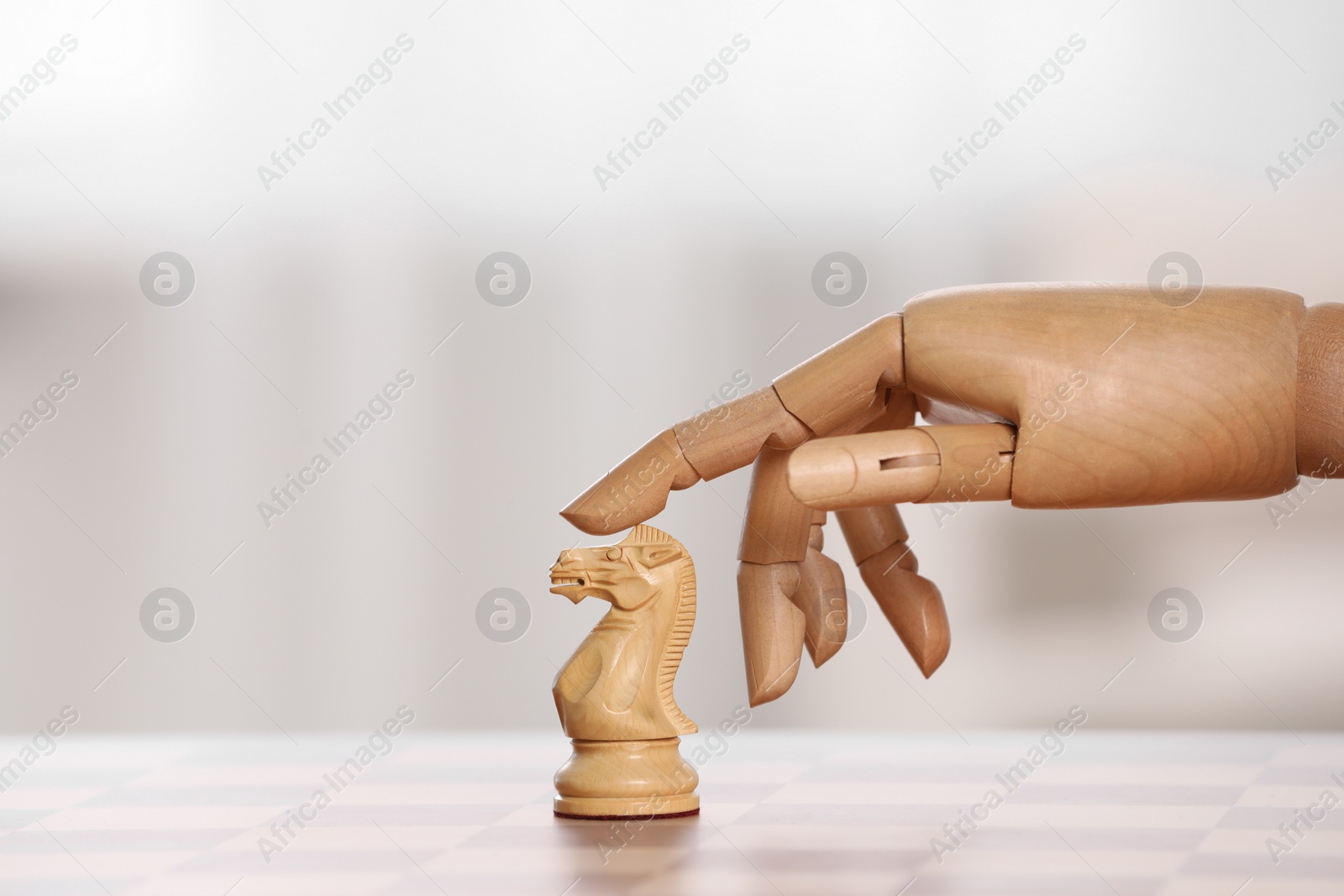 Photo of Wooden hand representing artificial intelligence. Robot touching knight on chessboard against light background, closeup