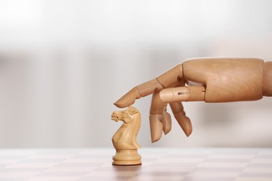 Wooden hand representing artificial intelligence. Robot touching knight on chessboard against light background, closeup