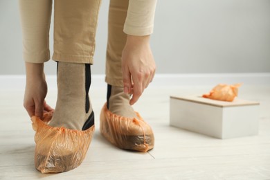 Woman wearing bright shoe covers onto her boots indoors, closeup