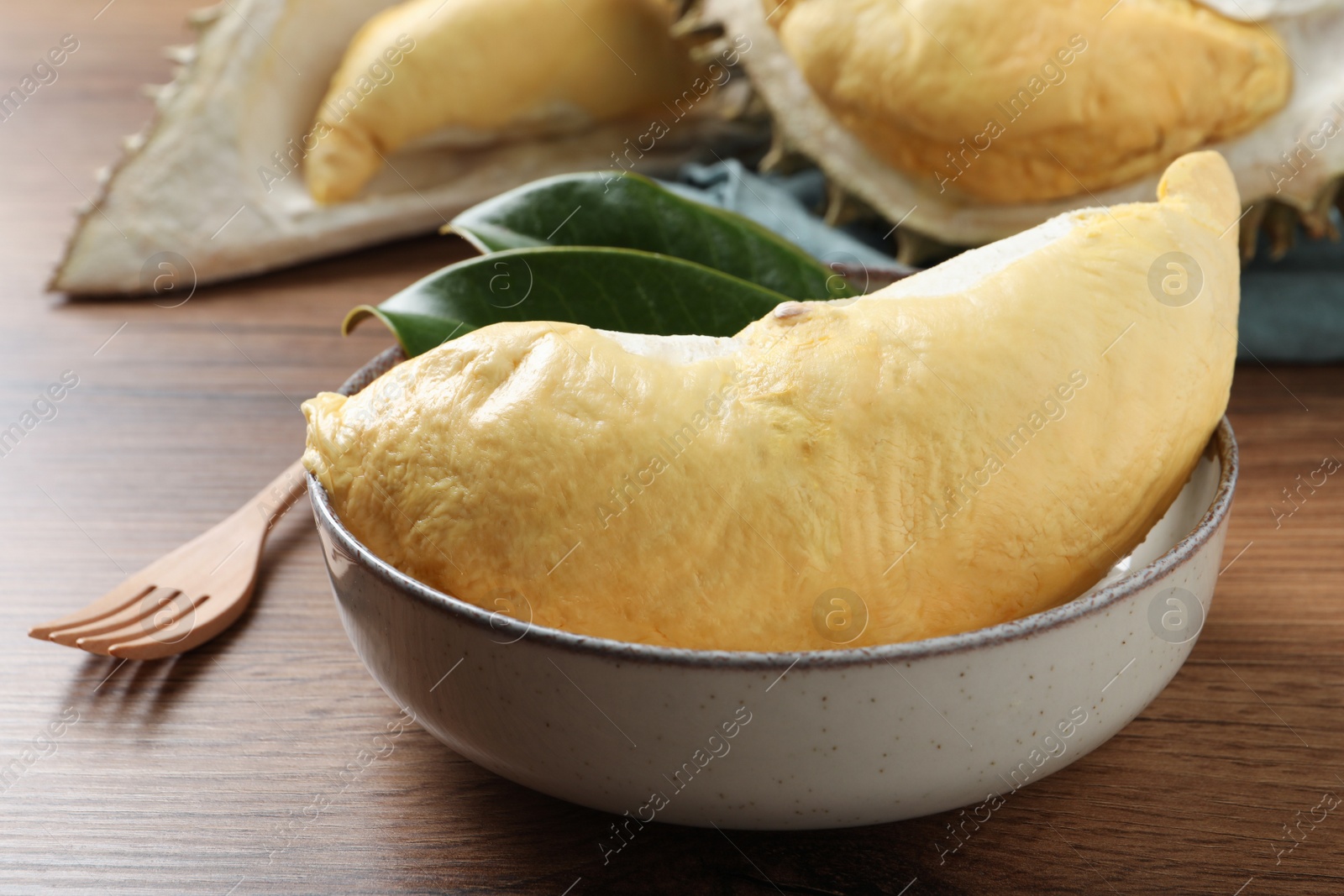 Photo of Bowl with piece of fresh ripe durian and leaves on wooden table, closeup