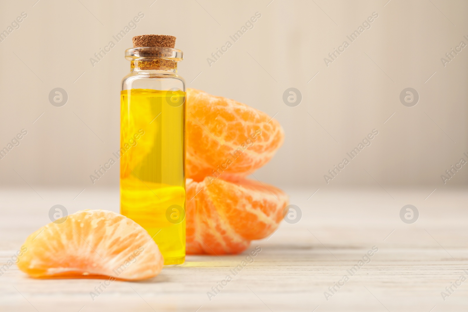 Photo of Bottle of tangerine essential oil and fresh fruit on white wooden table, closeup. Space for text