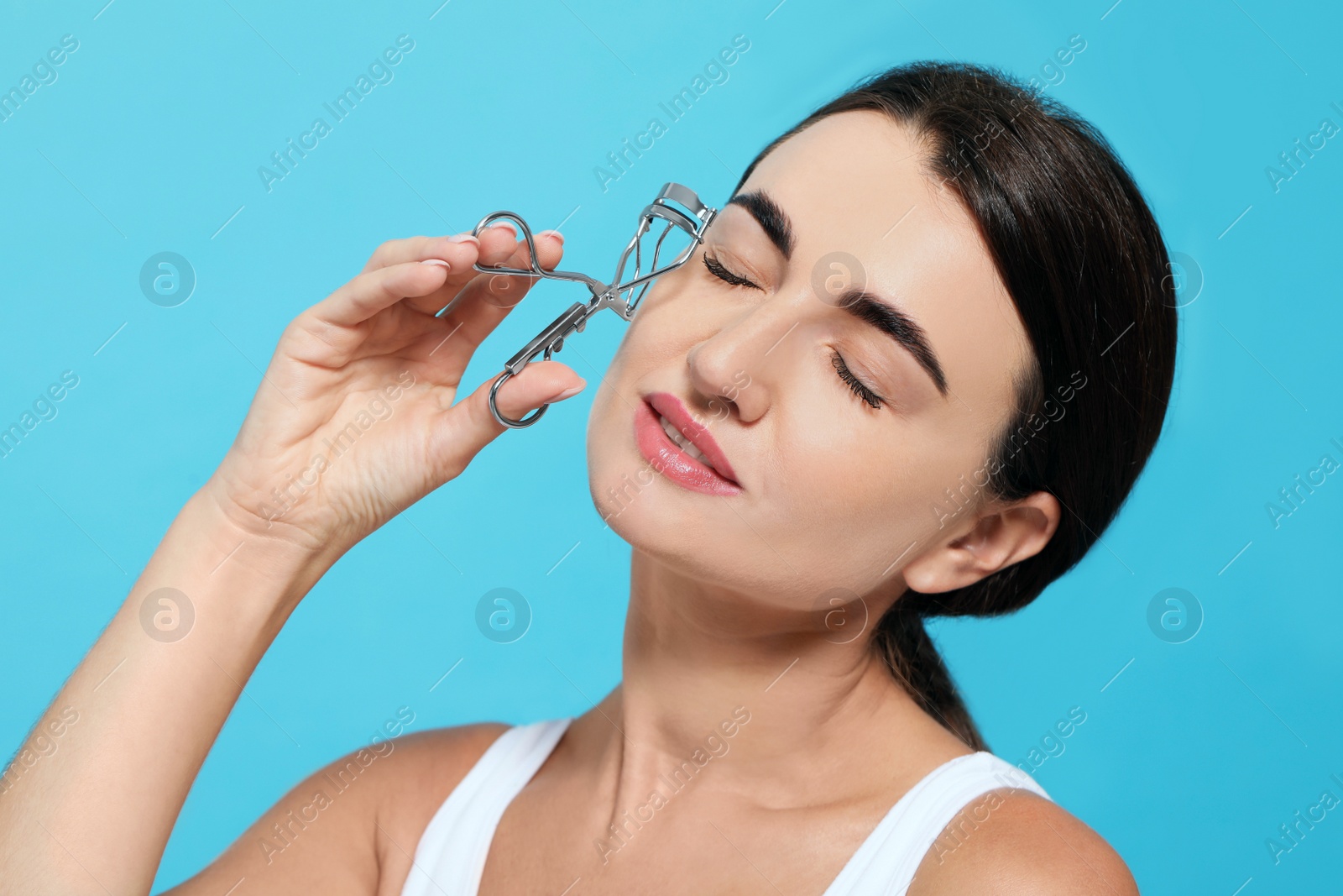 Photo of Woman with eyelash curler on turquoise background