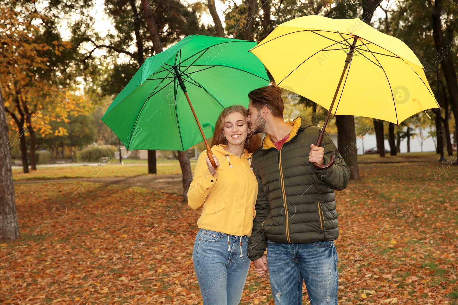 Photo of Happy couple with umbrellas walking in park