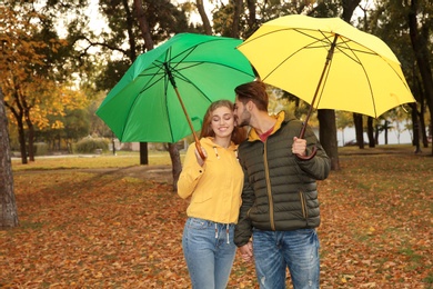 Happy couple with umbrellas walking in park