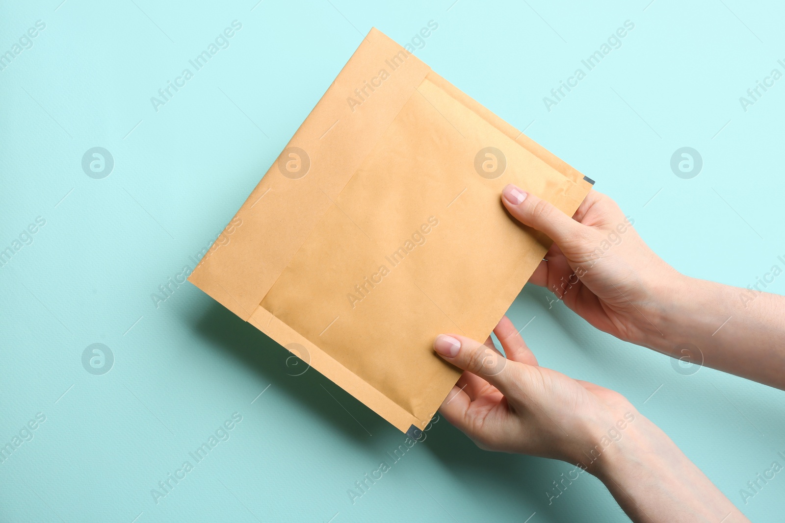 Photo of Woman holding kraft paper envelope on light blue background, closeup