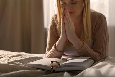 Religious young woman praying over Bible in bedroom