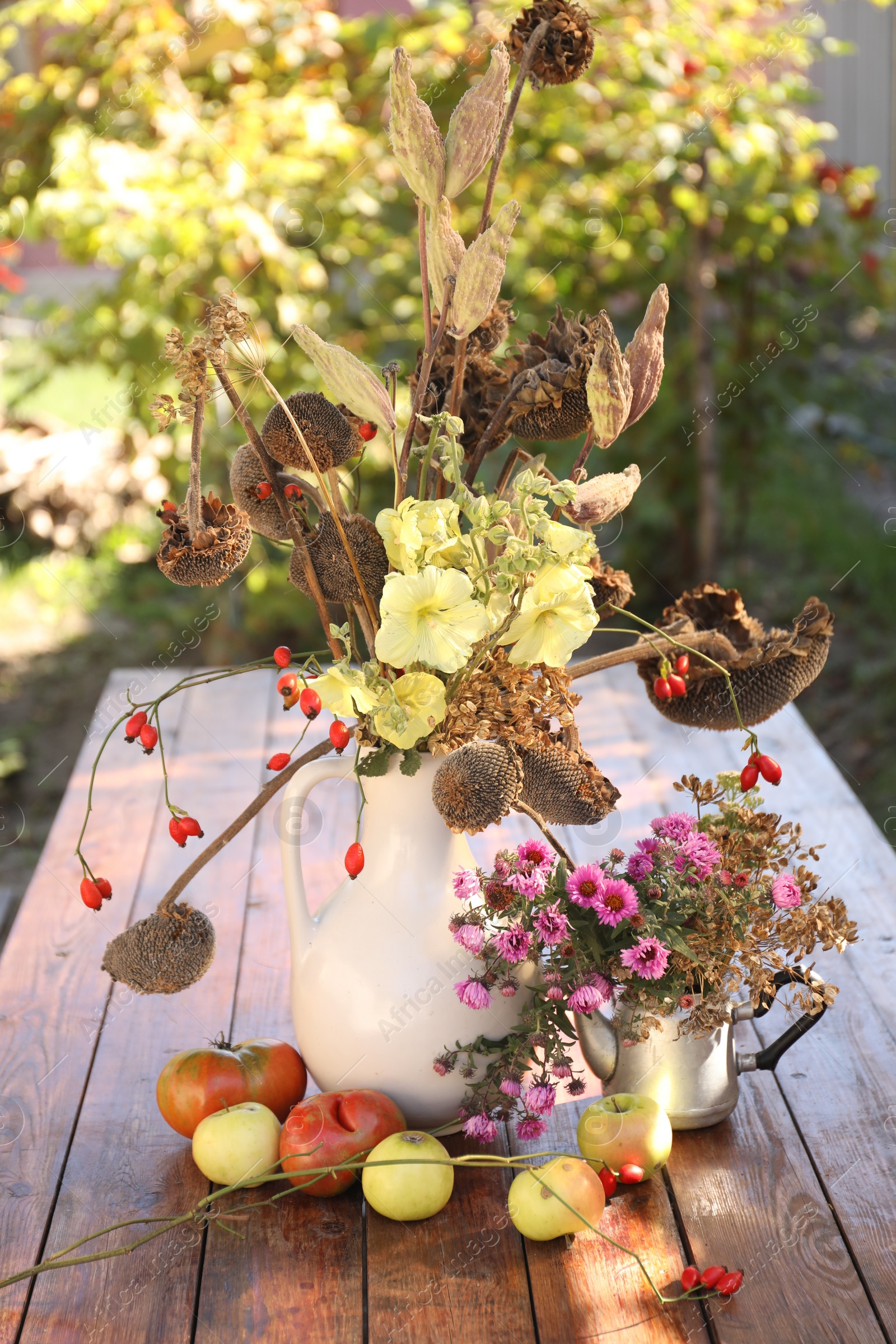 Photo of Composition with beautiful flowers, dry sunflowers and apples on wooden table outdoors. Autumn atmosphere