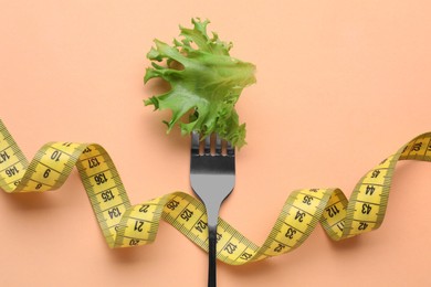 Fork with lettuce leaf and measuring tape on pale orange background, top view. Diet concept