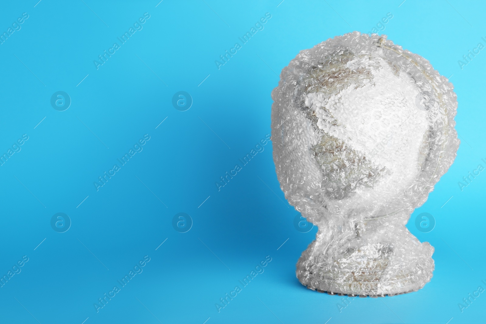 Photo of Globe packed in bubble wrap on turquoise background, space for text. Environmental conservation