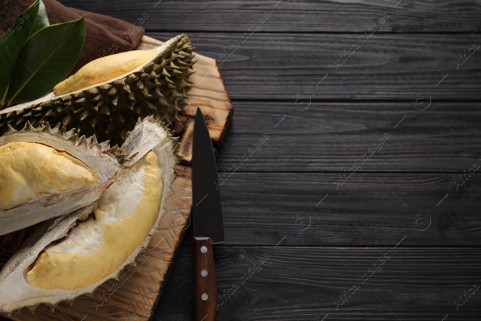 Photo of Pieces of fresh ripe durian and knife on black wooden table, top view. Space for text