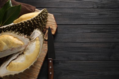 Photo of Pieces of fresh ripe durian and knife on black wooden table, top view. Space for text