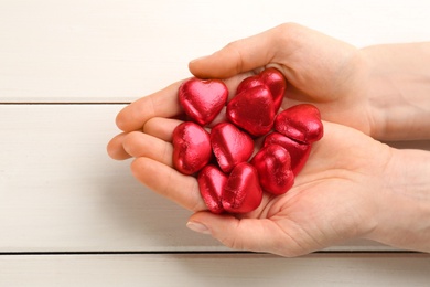 Woman holding heart shaped chocolate candies at white wooden table, top view