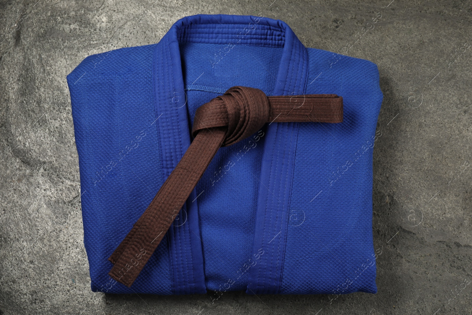 Photo of Brown karate belt and blue kimono on gray background, top view