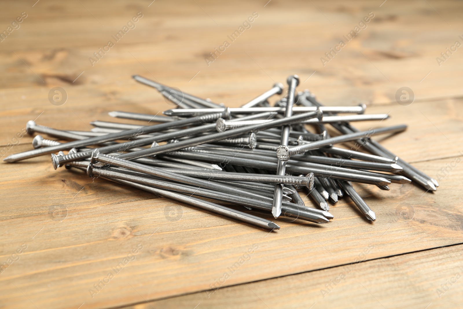 Photo of Pile of metal nails on wooden background, closeup