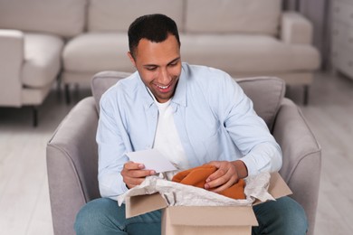 Photo of Happy man with greeting card near parcel at home. Internet shopping