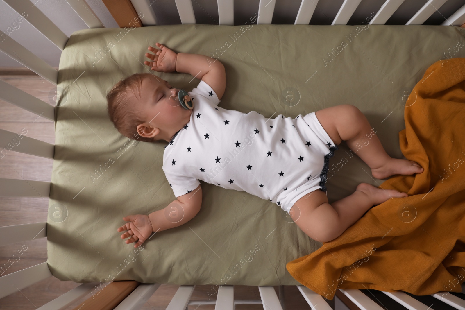 Photo of Adorable little baby with pacifier sleeping in crib indoors, top view