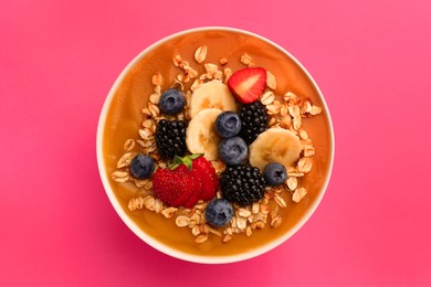 Photo of Delicious smoothie bowl with fresh berries, banana and oatmeal on pink background, top view