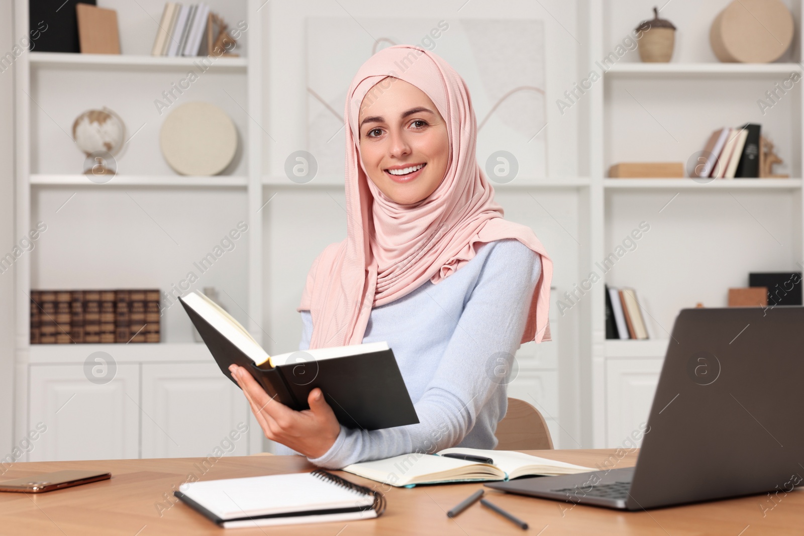 Photo of Muslim woman studying near laptop at wooden table in room