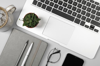 Modern laptop, stationery, cup of coffee, glasses, houseplant and smartphone on light grey table, flat lay