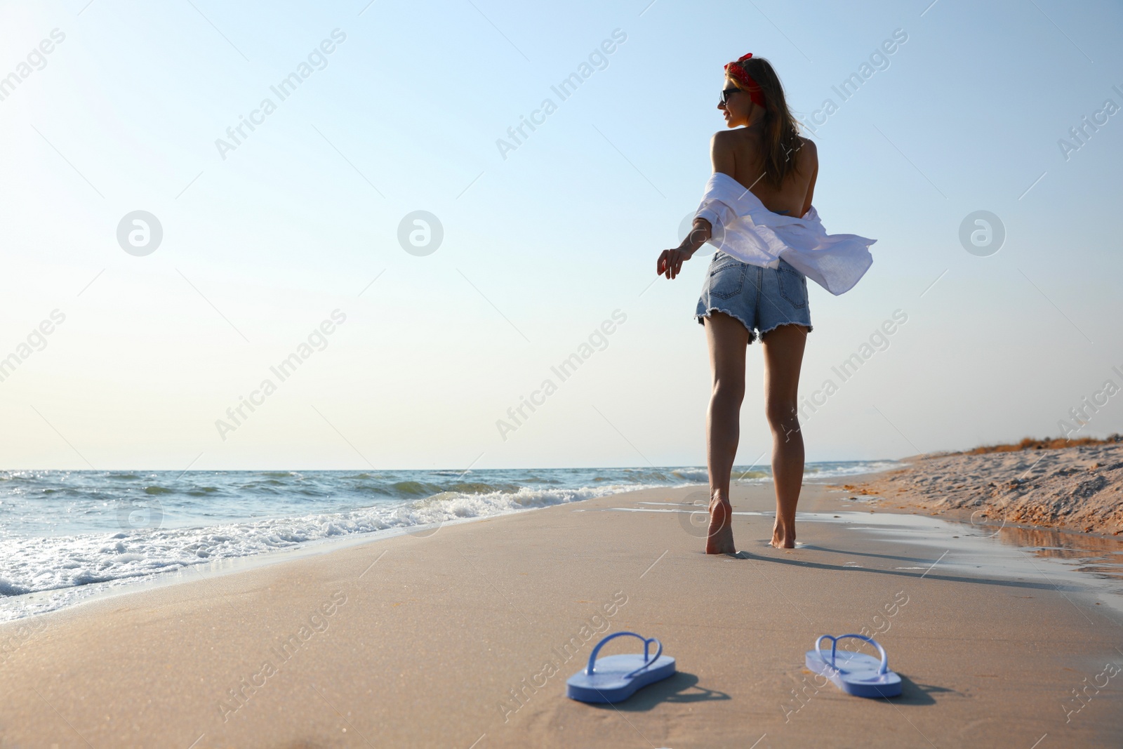 Photo of Woman left her beach slippers and walking barefoot on sandy seashore