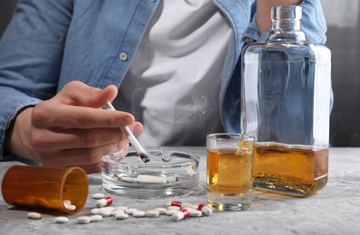 Photo of Alcohol and drug addiction. Man with smoldering cigarettes, whiskey and pills at grey textured table, closeup