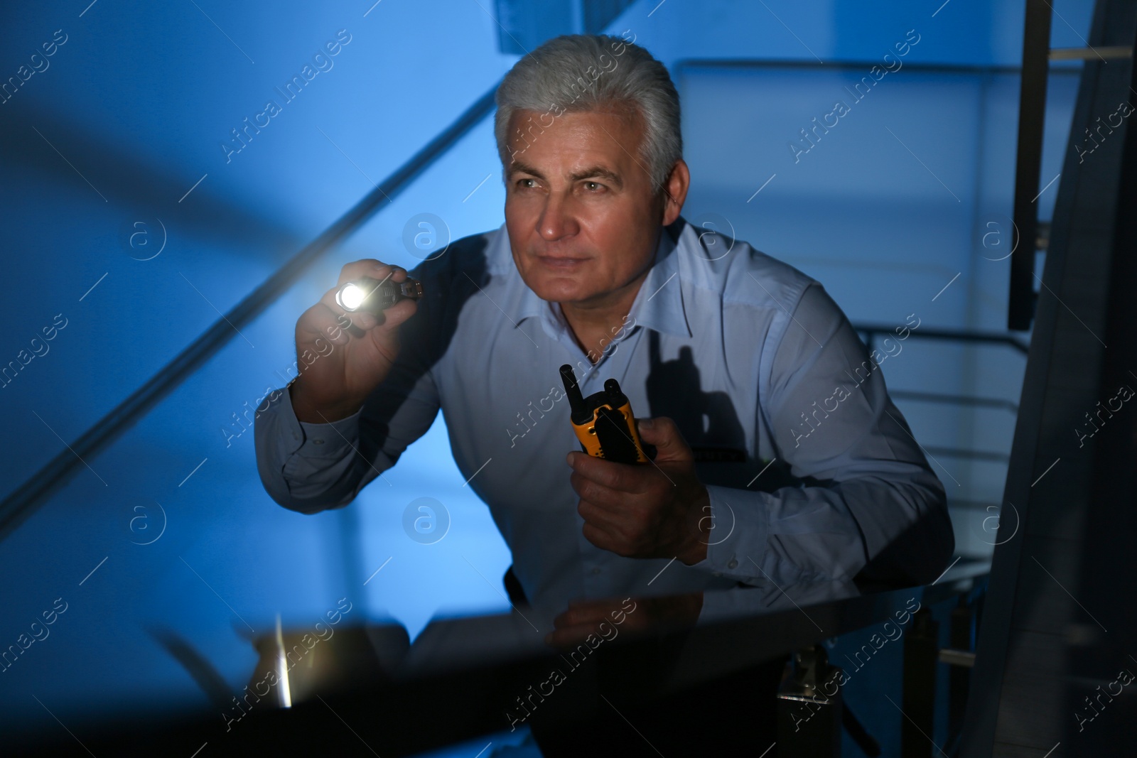 Photo of Professional security guard with flashlight on stairs in dark room