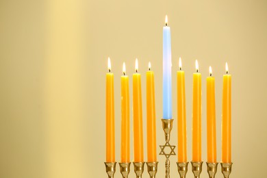 Hanukkah celebration. Menorah with burning candles on beige background, space for text