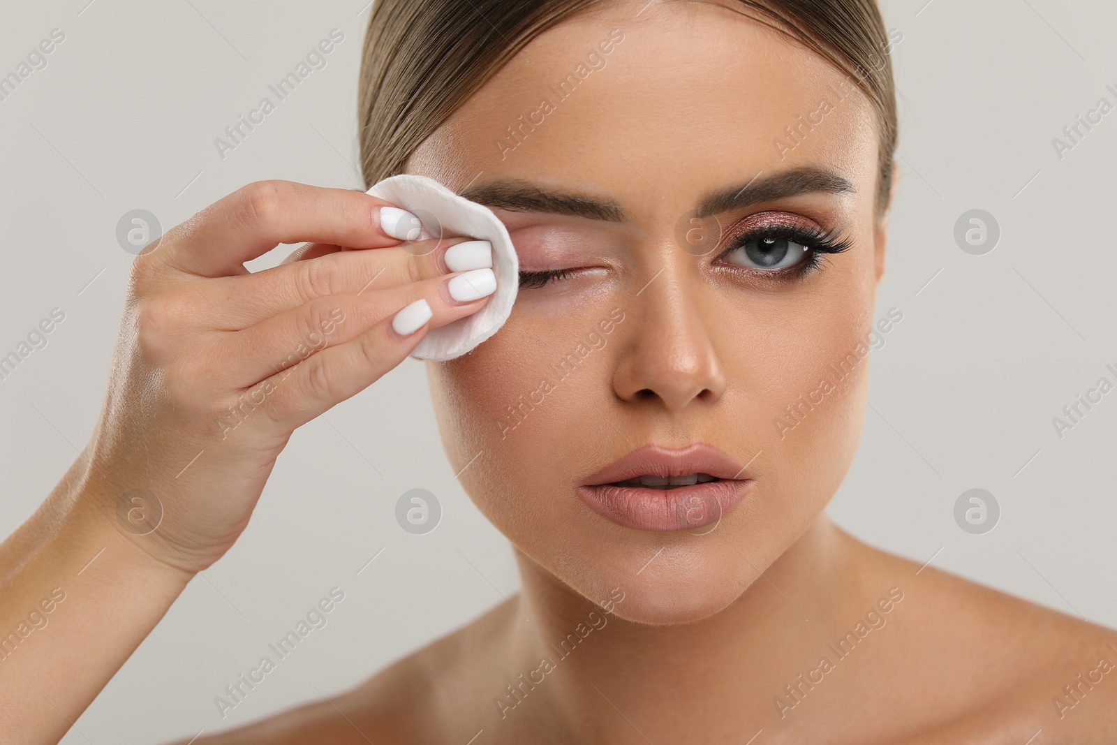 Photo of Beautiful woman removing makeup with cotton pad on light grey background, closeup