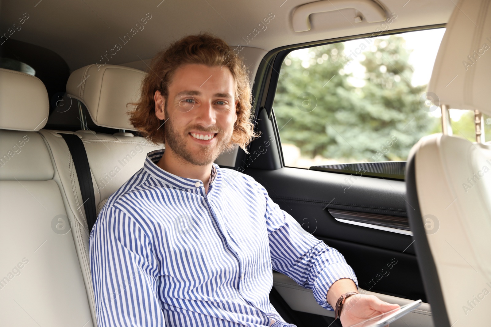 Photo of Attractive young man with tablet on backseat in luxury car