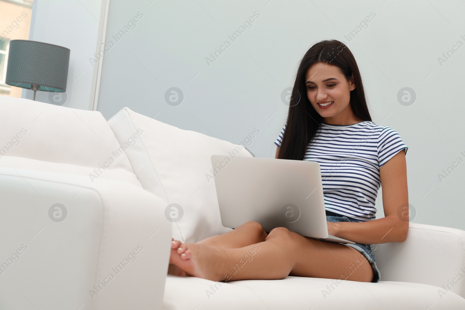 Photo of Young woman using laptop on sofa at home. Internet shopping