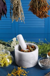 Mortar with pestle and many different herbs on blue wooden table, closeup