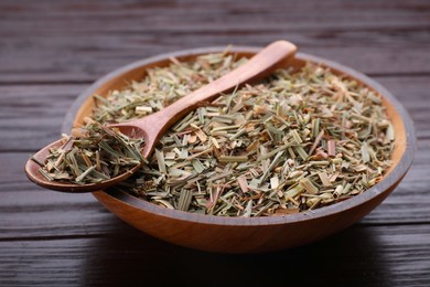 Photo of Bowl with aromatic dried lemongrass and spoon on wooden table, closeup