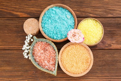 Bowls with sea salt and beautiful flowers on wooden table, flat lay