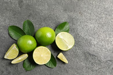 Photo of Fresh ripe limes and leaves on grey table, top view. Space for text