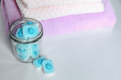 Photo of Jar with water softener tablets near stacked towels on table, space for text