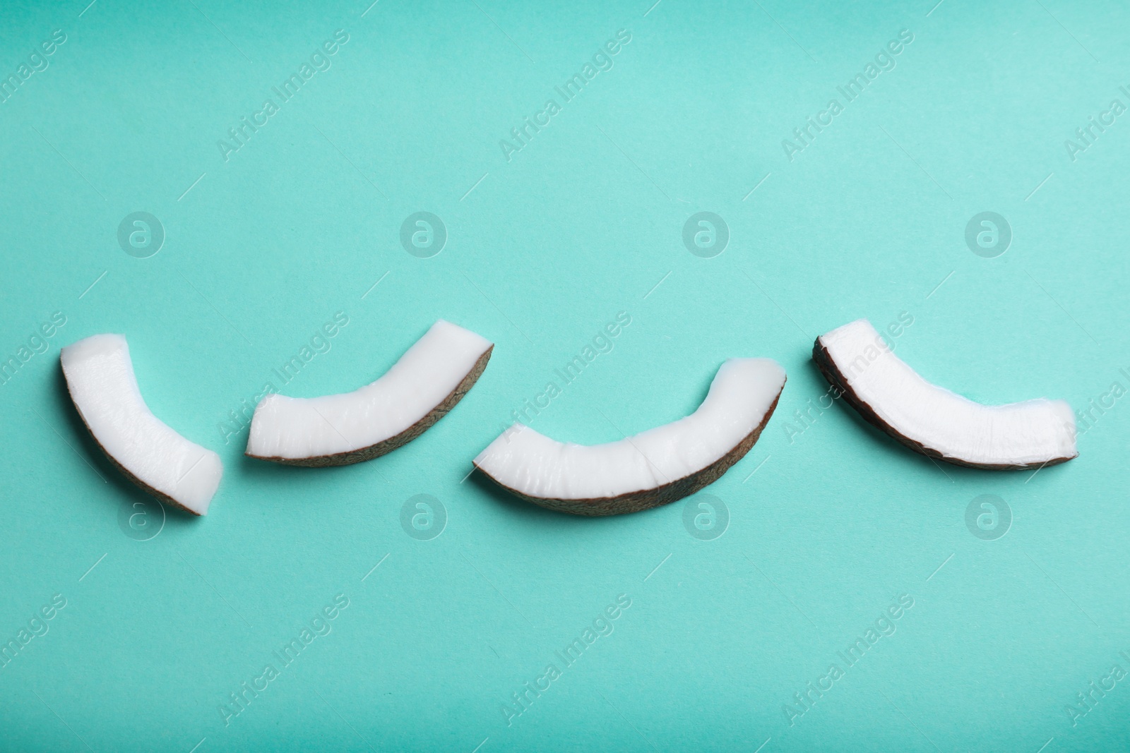 Photo of Fresh coconut pieces on turquoise background, flat lay