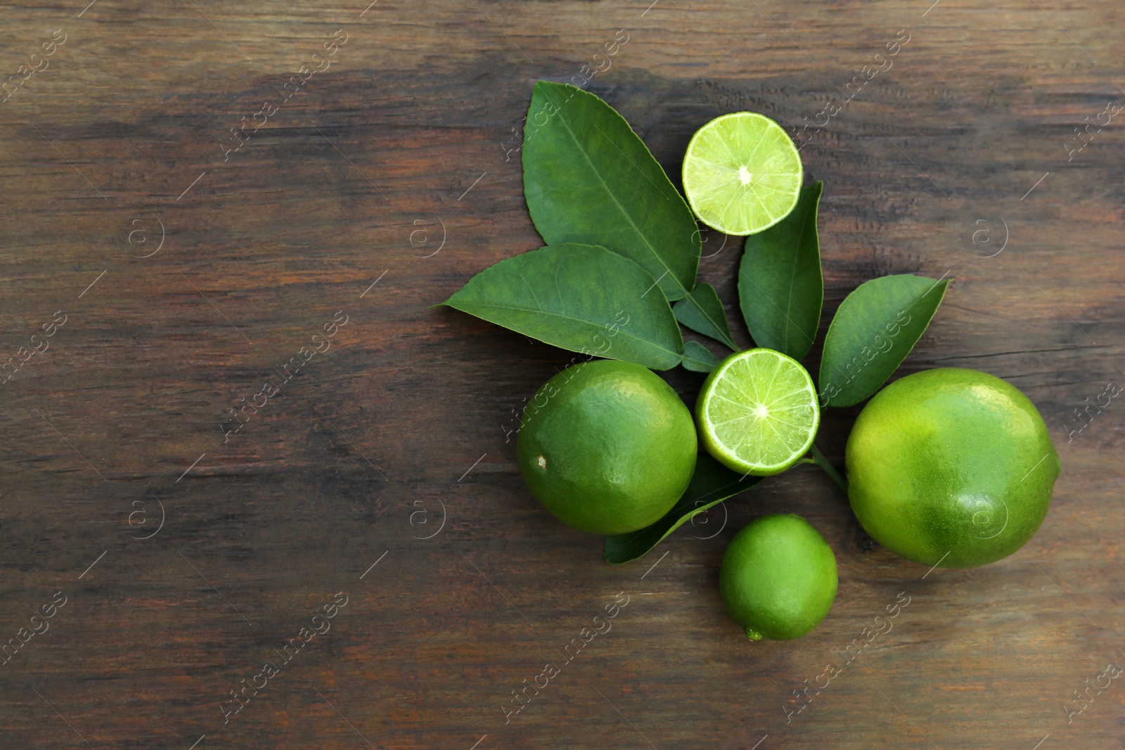 Photo of Whole and cut fresh ripe limes with green leaves on wooden table, flat lay. Space for text
