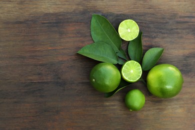 Photo of Whole and cut fresh ripe limes with green leaves on wooden table, flat lay. Space for text