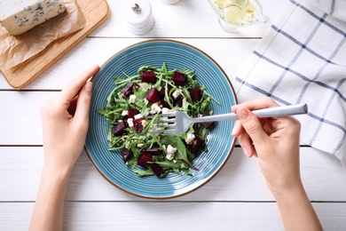 Woman eating fresh delicious beet salad at white wooden table, top view