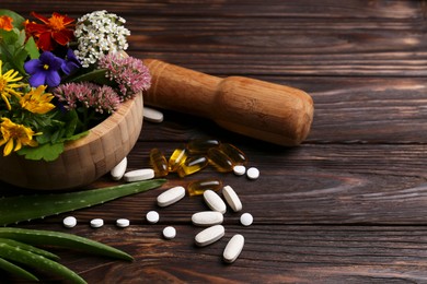 Photo of Mortar with fresh herbs, flowers and pills on wooden table, space for text