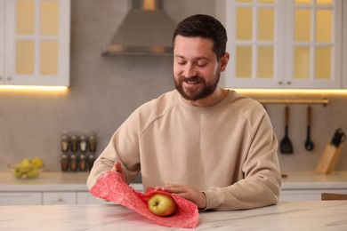 Man packing fresh apple into beeswax food wrap at table in kitchen
