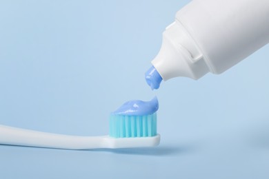 Applying paste on toothbrush against light blue background, closeup