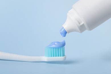 Photo of Applying paste on toothbrush against light blue background, closeup