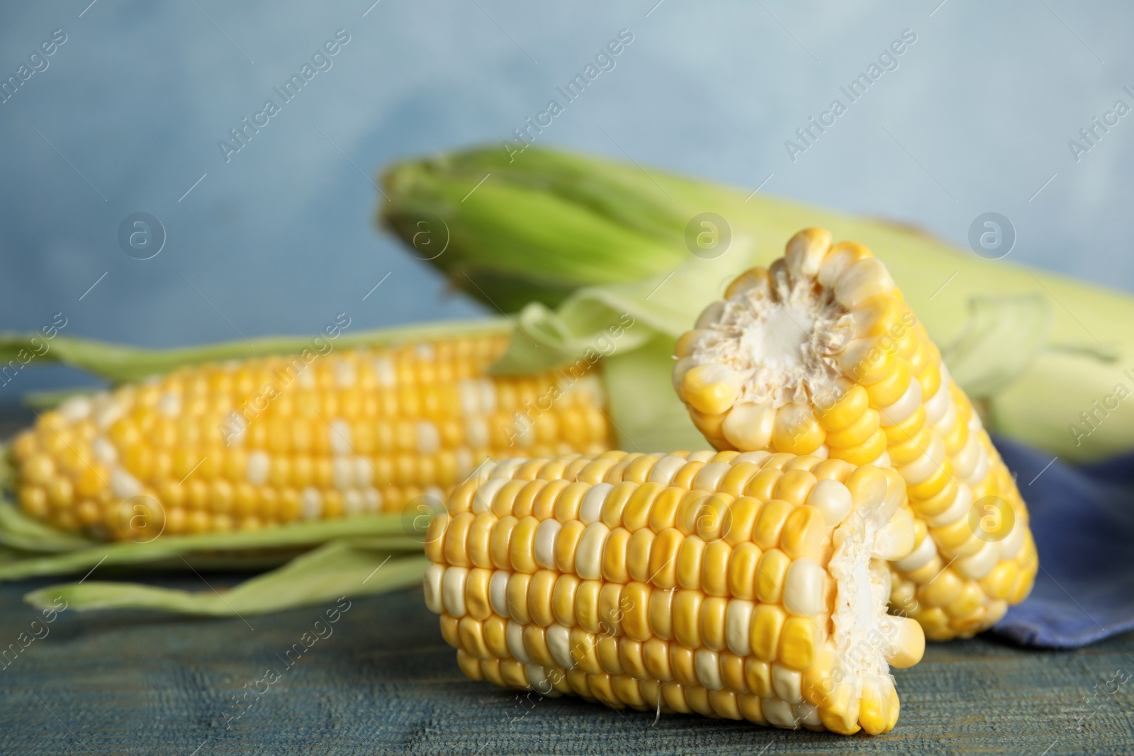 Photo of Tasty sweet corn cobs on blue wooden table, closeup view