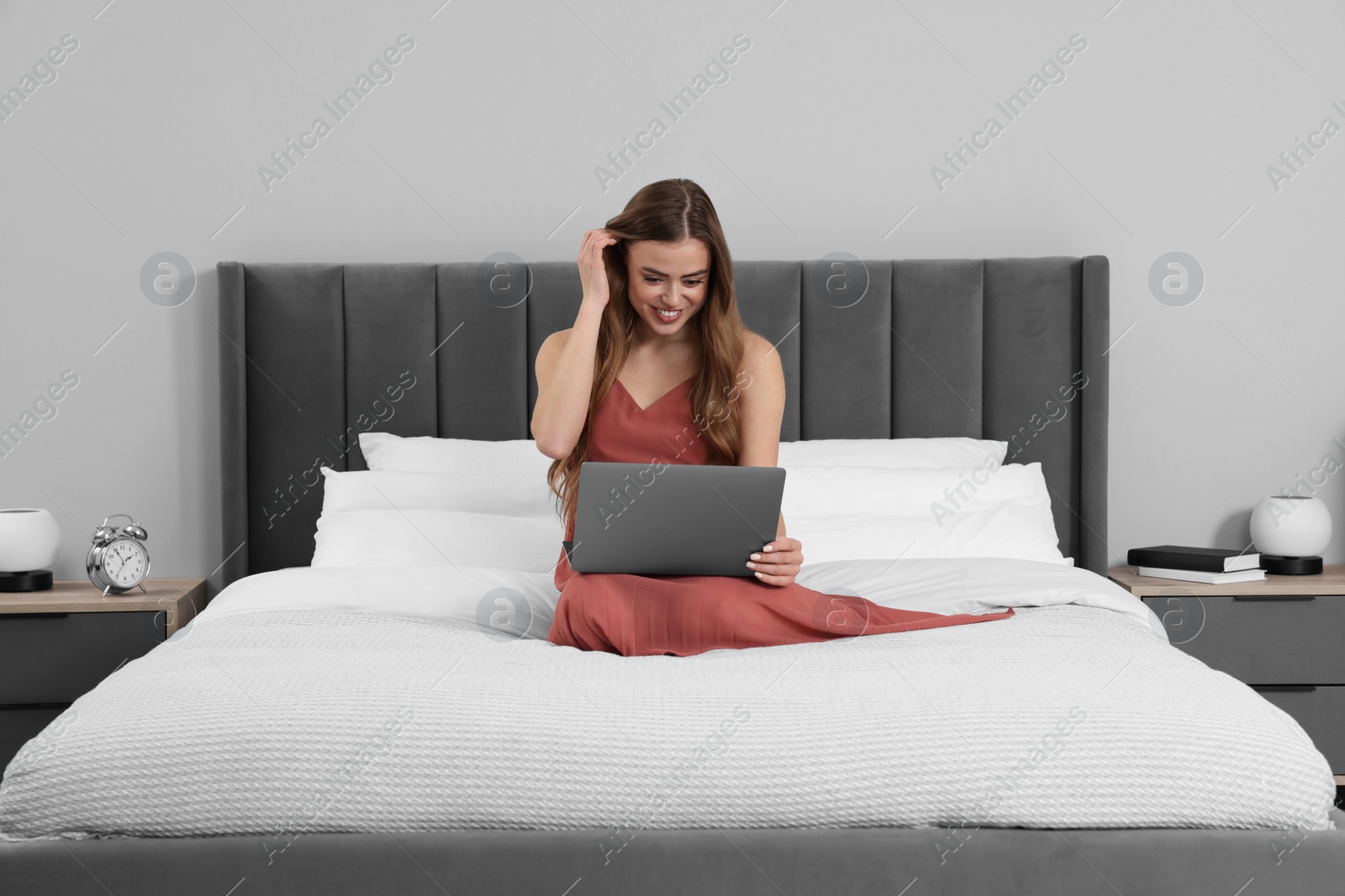 Photo of Happy woman with laptop on bed in bedroom