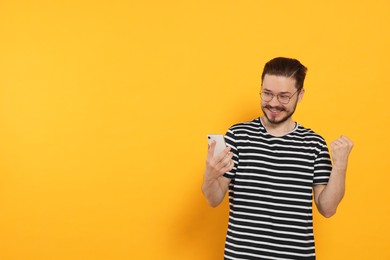 Emotional man with smartphone on orange background. Space for text