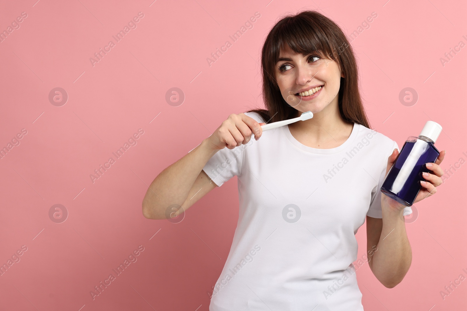 Photo of Young woman with mouthwash and toothbrush on pink background, space for text