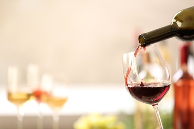 Photo of Pouring red wine from bottle into glass on blurred background. Space for text